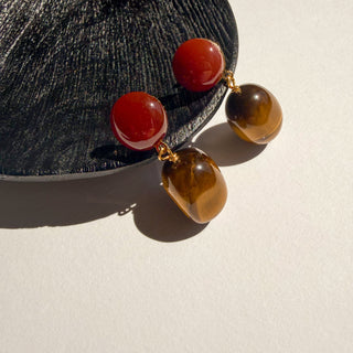 Boucles d’oreilles pendantes en pierres Youm, cornaline et œil de tigre, monture dorée à l’or fin 24k, oreilles percées et clips, photo posée.