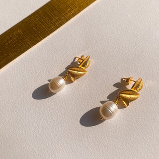 Boucles d’oreilles Capucine dorées, détail posé mettant en valeur les perles blanches, la texture et la finition dorée.