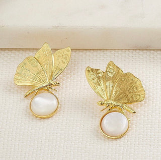 Boucles d’oreilles Chiara papillon dorées, détail posé mettant en valeur la nacre blanche, le motif papillon et la finition dorée.
