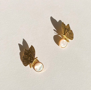 Boucles d’oreilles Chiara papillon dorées, zoom détail posé mettant en valeur la nacre blanche, le motif papillon et la finition dorée.