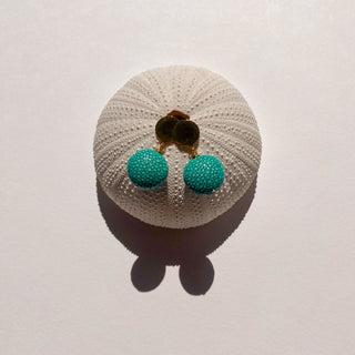Boucles d’oreilles Gala en galuchat turquoise, détail posé mettant en valeur la texture du galuchat et la finition dorée à l’or fin 24 carats, pour oreilles percées ou clips.