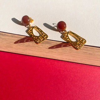 Boucles d’oreilles Gustave dorées style Art Déco, détail posé mettant en valeur la pierre cornaline, les lignes géométriques et la finition dorée, pour oreilles percées ou clips non percées.