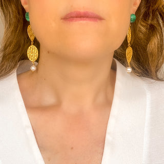 Boucles d’oreilles Liz XXL dorées en malachite et perles naturelles portées vue de face, montrant la longueur, le mouvement et l’éclat des pierres, disponibles en percées ou clips.