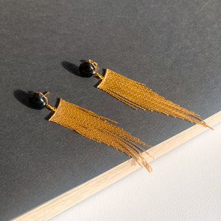 Boucles d’oreilles Niagara pendantes dorées, détail posé mettant en valeur l’agate noire, la texture et la finition dorée. Disponibles en version oreilles percées ou non percées clips.