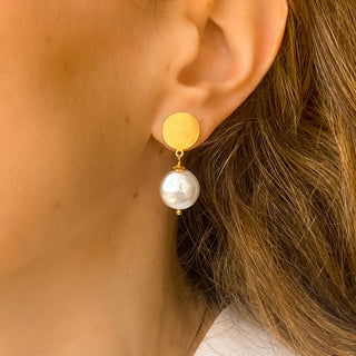 Boucles d’oreilles Pernille pendantes dorées avec perle blanche portées de profil, montrant la longueur de 3,5 cm, l’éclat de la dorure et la taille de la perle (~1,8 cm), disponibles en percées ou clips.