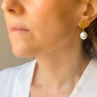 Boucles d’oreilles Pernille pendantes dorées avec perle blanche portées, montrant la longueur de 3,5 cm, l’éclat de la dorure et la taille de la perle (~1,8 cm), disponibles en percées ou clips.