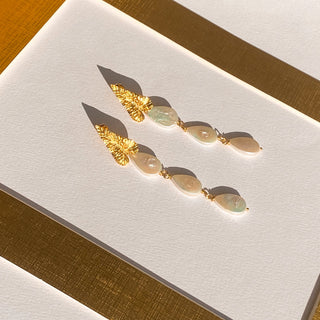 Boucles d’oreilles Zephyr pendantes dorées, détail posé mettant en valeur les perles blanches naturelles et la finition dorée.