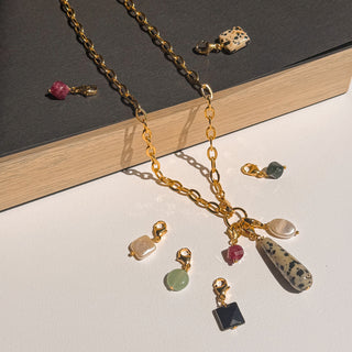 Collier charms personnalisable doré Youm avec charms posé à plat, composition harmonieuse mettant en valeur les pierres naturelles.