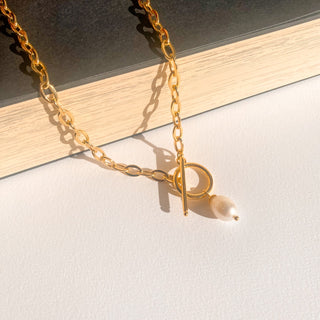 Zoom sur le collier doré Izia avec une perle blanche.