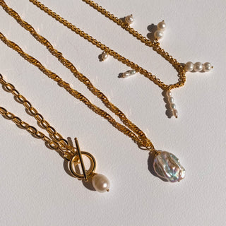 Collection de colliers dorées avec des perles blanches.