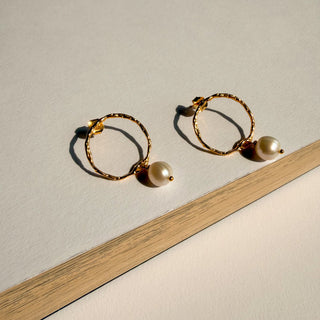 Boucles d’oreilles Diego petit cercle doré avec perle blanche Youm, finition or fin 24 carats, posé pour le montrer le détail de la boucle d'oreille.