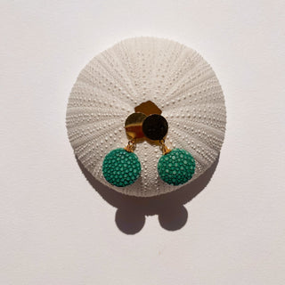 Boucles d’oreilles Gala vert posées à plat, lumière douce, mettant en valeur la texture galuchat et la finition dorée mate.