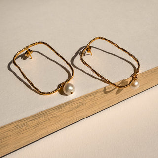 Boucles d’oreilles Luis grand rectangle doré avec perle blanche Youm, finition or fin 24 carats, pose pour montrer le détail de la boucle d'oreille et de la perle.