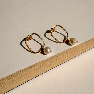 Boucles d’oreilles Nils petit rectangle doré avec perle blanche Youm, finition or fin 24 carats, posé pour montrer le détail de la perle blanche et de la dorure.