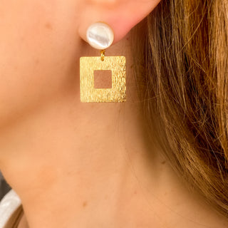 Boucles d’oreilles Claude dorées en nacre blanche portées, montrant la forme graphique, l’éclat de la nacre et la finesse du design, disponibles en percées ou clips.