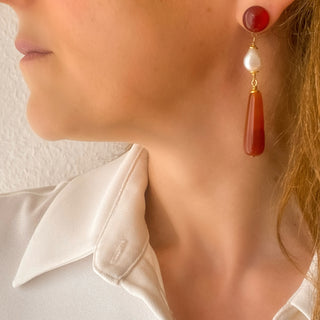 Boucles d’oreilles Clémentine pendantes dorées en cornaline, agate rouge et perles blanches portées, montrant la longueur, les couleurs chaudes des pierres naturelles et l’éclat de la dorure, disponibles en percées ou clips. 