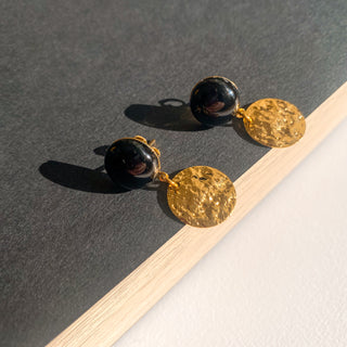 Boucles d’oreilles Doris pendantes dorées, détail posé mettant en valeur la pierre d’agate noire, la texture et la finition dorée.