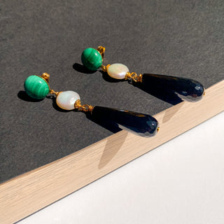 Boucles d’oreilles Felix pendantes dorées, détail posé mettant en valeur la malachite verte, la perle naturelle, l’onyx noir et la finition dorée, pour oreilles percés et clips.