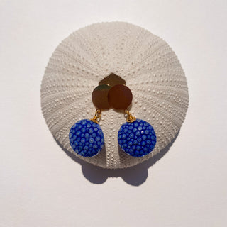 Boucles d’oreilles Gala en galuchat bleu, détail posé mettant en valeur la texture du galuchat et la finition dorée à l’or fin 24 carats.