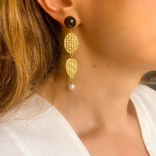 Boucles d’oreilles Liz pendantes dorées en agate noire et perles naturelles portées de profil, montrant la longueur, le mouvement et le contraste des pierres, disponibles en percées ou clips.