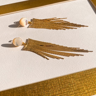 Boucles d’oreilles Niagara pendantes dorées, détail posé mettant en valeur la nacre blanche, la texture et la finition dorée, disponibles en percées ou clips.