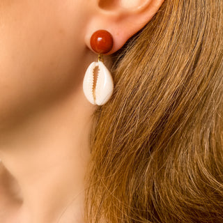 Boucles d’oreilles Océane dorées en coquillage cauri et jaspe rouge portées, montrant la longueur, le mouvement et l’esprit été, disponibles en percées ou clips.