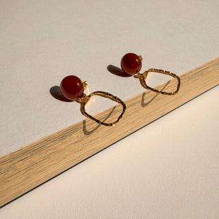 Boucles d’oreilles pendantes Curt petit rectangle doré avec cornaline Youm, finition or fin 24 carats, pour oreilles percées ou clips, photo posée pour montrer le détail de la pierre et la dorure.