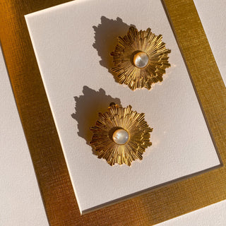 Boucles d’oreilles Soléa clips dorées à l’or fin 24 carats, détail posé mettant en valeur le motif soleil et la nacre blanche.