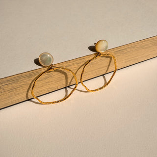 Boucles d’oreilles Thomas cercle doré avec nacre blanche Youm, finition or fin 24 carats, disponible pour oreilles percées ou clips,  photo posée pour montrer le détail de la boucle d'oreille.