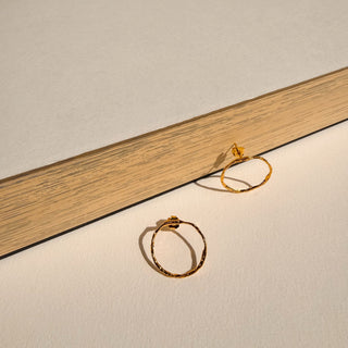 Boucles d’oreilles Tiago rond doré Youm, finition or fin 24 carats, posé pour montrer la dorure du bijou.