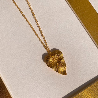 Collier feuille Celian Youm posé à plat, lumière douce, mettant en valeur le pendentif feuille doré.