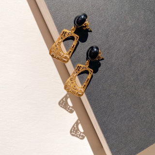 Boucles d’oreilles Gustave dorées, détail posé mettant en valeur la pierre naturelle d’agate noire, la structure Art Déco et la finition en or fin 24 carats, pour oreilles percées et clips.