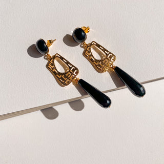 Boucles d’oreilles Gustave L dorées, détail posé mettant en valeur les pierres d'agate noire, l’onyx et la finition en or fin 24 carats dans un design Art Déco.