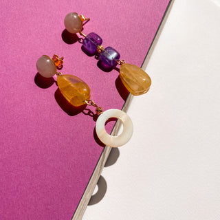 Boucles d’oreilles dépareillées Noémie dorées, détail posé mettant en valeur les pierres naturelles colorées, l’asymétrie et la finition dorée.