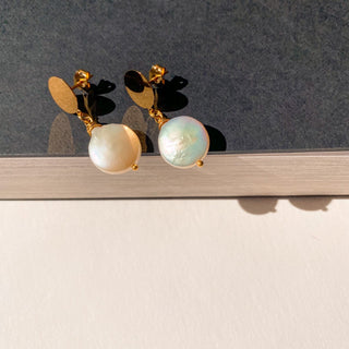 Boucles d’oreilles Pernille dorées, détail posé mettant en valeur la perle blanche, la finition en or fin 24 carats et le système percé ou clip.