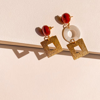 Boucles d’oreilles Arielle dépareillées dorées, détail posé mettant en valeur la cornaline, la nacre blanche et la finition en or fin 24 carats.