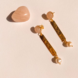 Boucles d’oreilles Cleo dorées, détail posé mettant en valeur le quartz rose, les perles blanches et la finition en or fin 24 carats. 