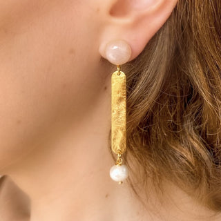 Boucles d’oreilles Cleo pendantes dorées en quartz rose et perles blanches portées, montrant la longueur, l’éclat de la dorure et la douceur des pierres naturelles, disponibles en percées ou clips.