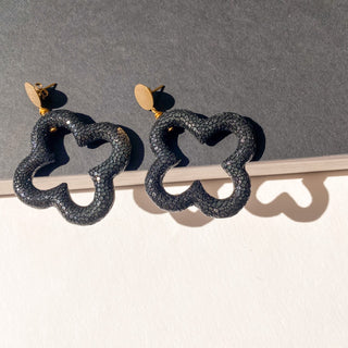 Boucles d’oreilles Trèfle en galuchat noir, zoom posé mettant en valeur la texture du galuchat, la forme trèfle et la finition dorée à l’or fin 24 carats.