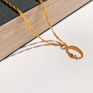 Collier serpent Loa doré, détail posé mettant en valeur le pendentif serpent, la texture et la finition en or fin 24 carats.