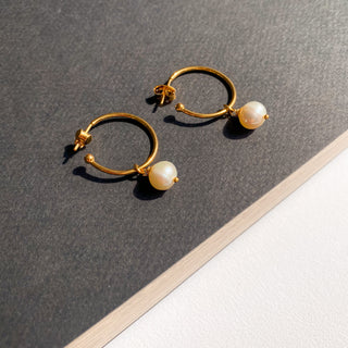 Créoles Jane dorées avec perle blanche naturelle, détail posé mettant en valeur la perle ronde et la finition dorée à l’or fin 24 carats.